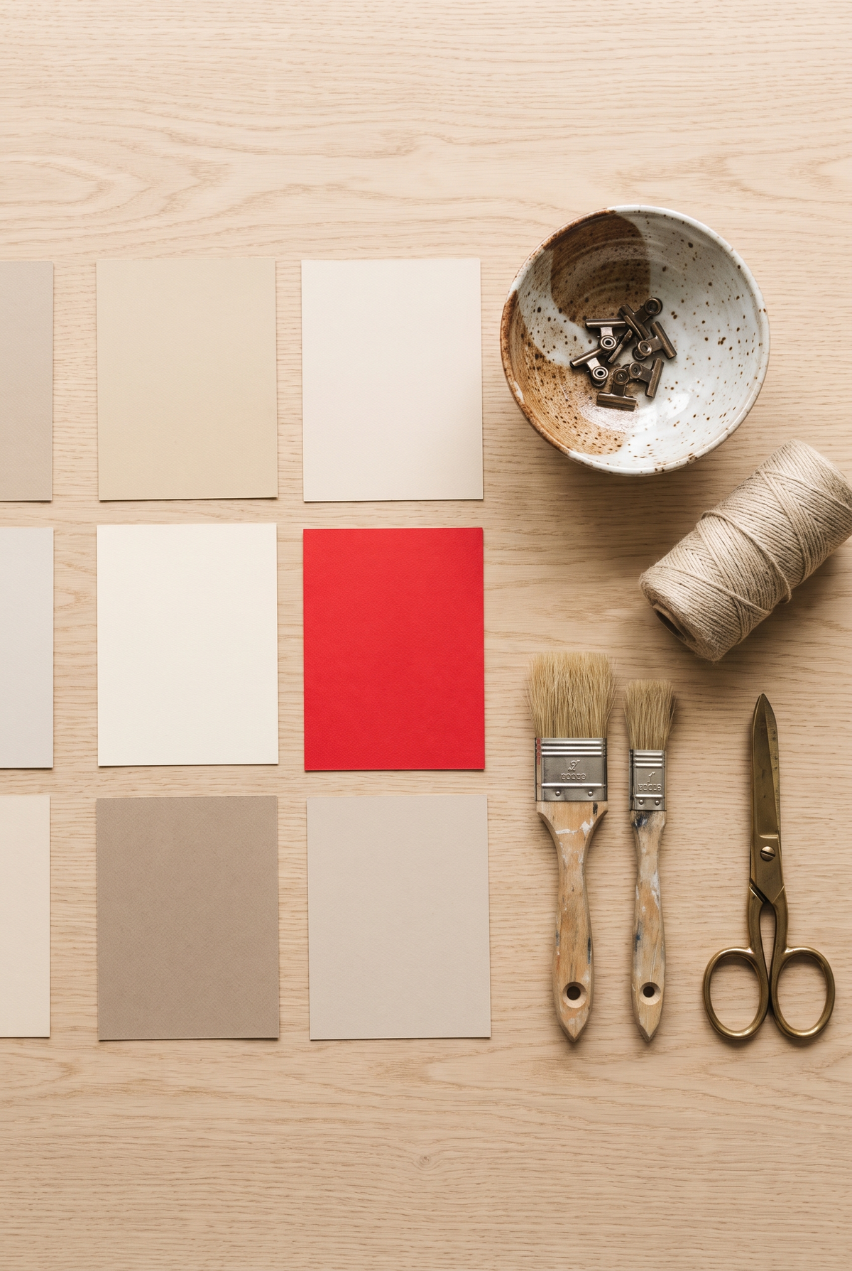 Paper color swatches, a ceramic bowl, linen thread and brushes on a craft workbench